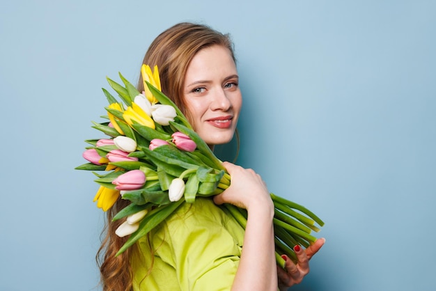 Portret kobiety z bukietem kwiatów tulipanów na czystym niebieskim tle
