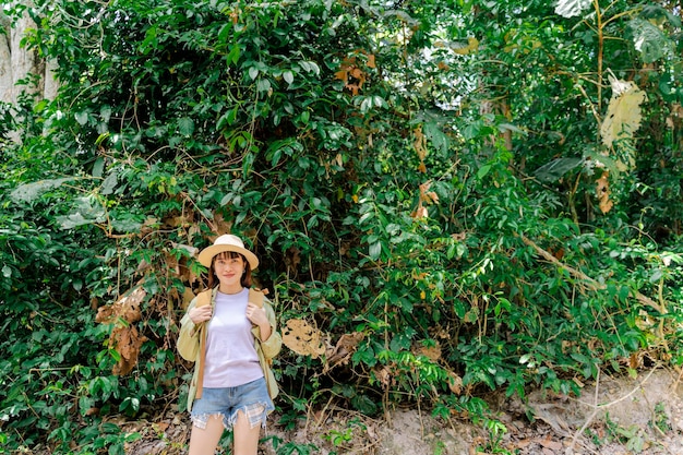 Portret kobiety z plecakiem i słomkowym kapeluszem w lesie uśmiechnięta dziewczyna na wycieczce letni trekking szczęśliwa kobieta ciesząca się spacerem po górze