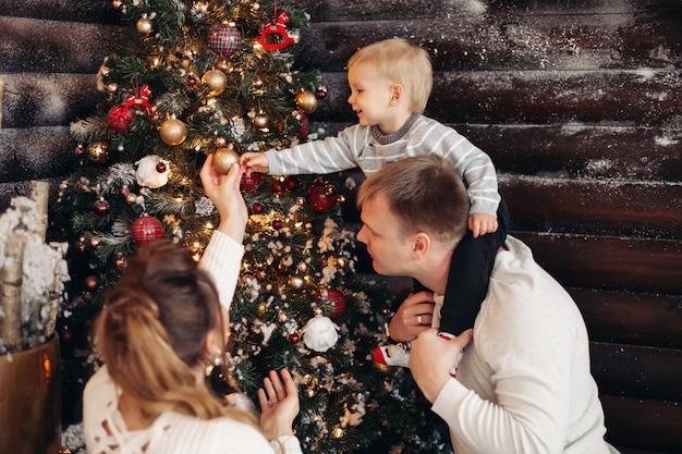 Portret kochającego taty z córką na ramionach przy dekorowaniu pięknej choinki zabawkami i dekoracjami w domu
