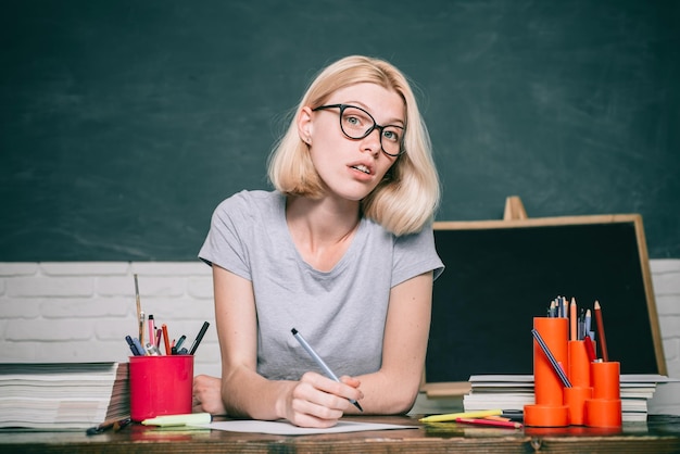 Portret kreatywna młoda uśmiechnięta studentka w okularach młoda kobieta siedząca przy stole robi asy...