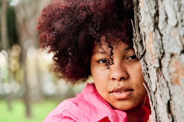 Portret kręconej Afroamerykanki opartej o drzewo