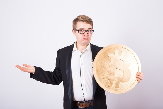 Portret krzyczącego biznesmena trzyma w ramionach duże złote bitcoiny. Mężczyzna w panice z powodu awarii kryptowaluty.