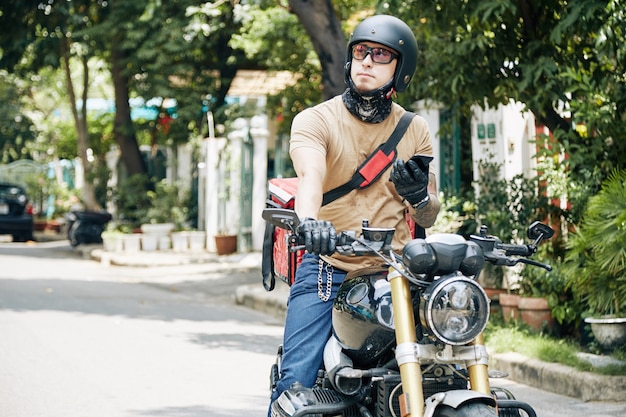 Portret kuriera na motocyklu rozglądającego się w poszukiwaniu domu klienta