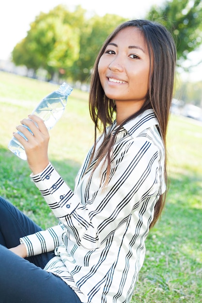 Zdjęcie portret ładnej azjatyckiej dziewczyny w parku z butelką wody