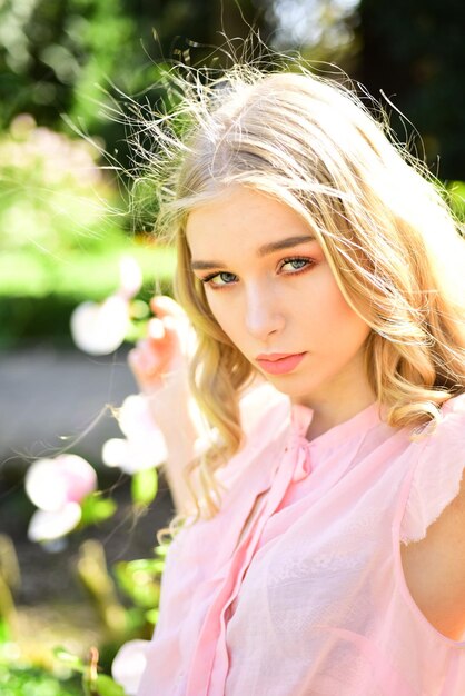 Portret ładnej blond dziewczyny na naturalnym tle Młoda dziewczyna z zakręconymi złotymi lokami ubrana w różową bluzkę pozuje w kwitnącym ogrodzie w słoneczny dzień