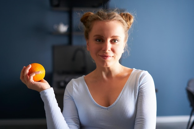 Portret ładnej buźki kaukaskiej dziewczyny trzymającej całą świeżą soczystą pomarańczę stojącą w domu w niej