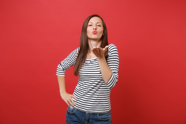 Portret ładnej, delikatnej młodej kobiety w pasiastych ubraniach, stojącej, całującej, wysyłającej buziaka powietrznego