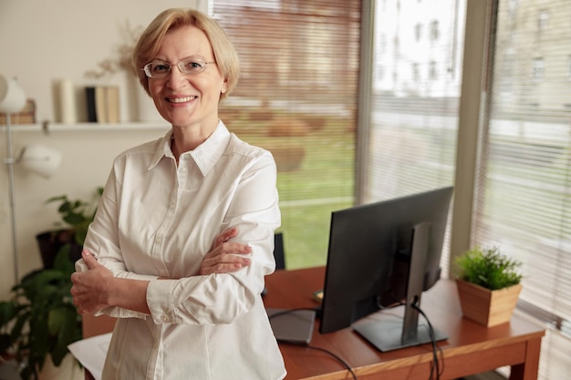 Portret ładnej dojrzałej kobiety freelancer w okularach stojącej na tle biura domowego