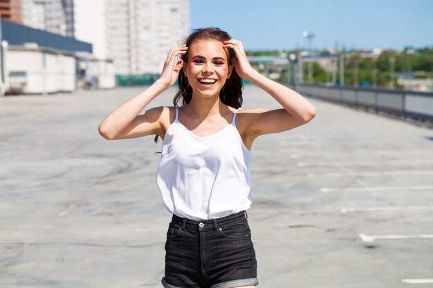 Zdjęcie portret ładnej młodej brunetki w białej letniej bluzce i dżinsach idącej po letniej ulicy na świeżym powietrzu