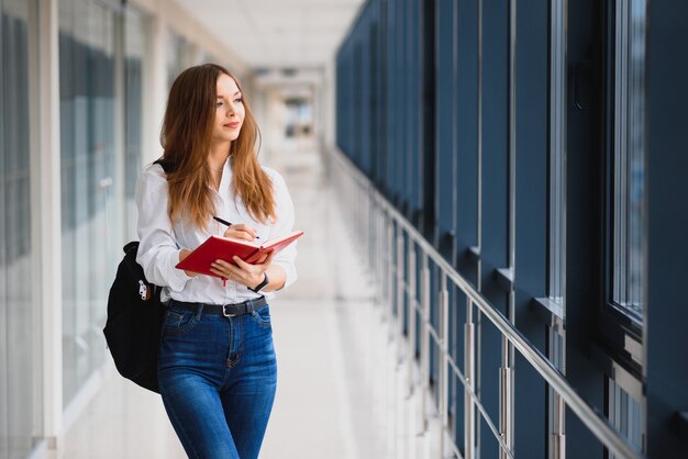 Portret ładnej studentki z książkami i plecakiem na korytarzu uniwersytetu