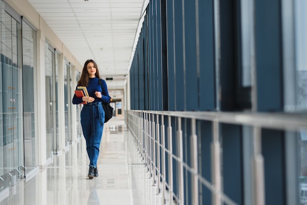 Portret ładnej studentki z książkami i plecakiem na korytarzu uniwersytetu