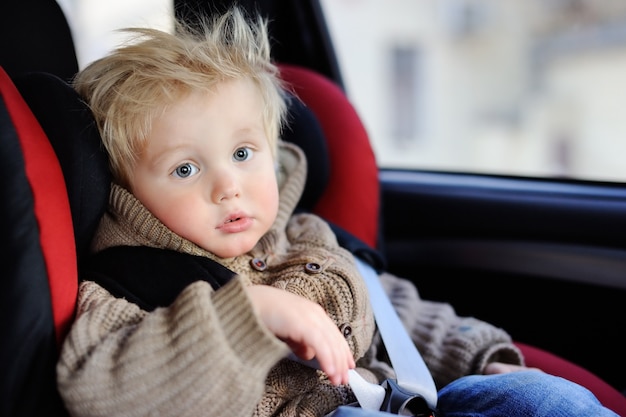 Portret ładny chłopiec maluch siedzi w foteliku samochodowym. Bezpieczeństwo transportu dzieci