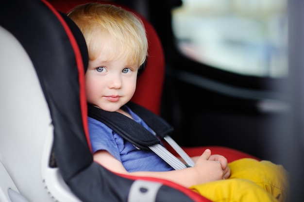 Portret ładny chłopiec maluch siedzi w foteliku samochodowym. Bezpieczeństwo transportu dzieci