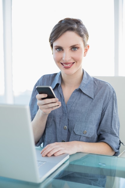 Portret ładny spokojny bizneswoman trzyma jej smartphone obsiadanie przy jej biurkiem