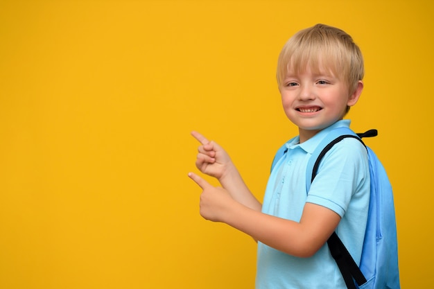 Portret ładny uczeń z jasnym plecakiem na żółtej ścianie.