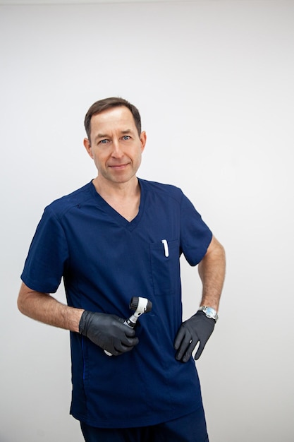 Portret lekarza kosmetologa w niebieskim mundurze medycznym i czarnych rękawiczkach z dermatoskopem w dłoniach