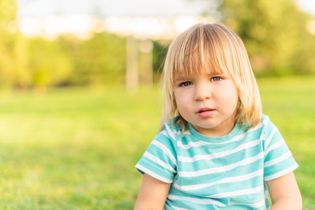 Portret Małego Blond Chłopca Patrzącego Na Kamerę Siedzącego Na Trawie W Parku Z Miejscem Na Kopię I Rozmytym Tłem Selektywna Ostrość