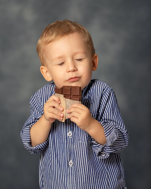 Portret małego chłopca jedzącego czekoladę na szarym tle Szczęśliwy koncept dzieciństwa Słodki ząb