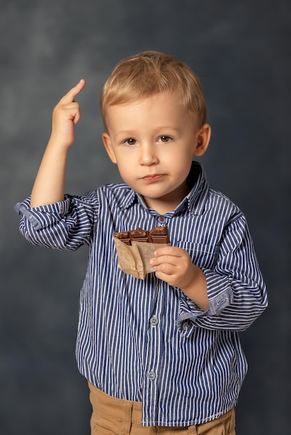 Zdjęcie portret małego chłopca jedzącego czekoladę na szarym tle szczęśliwy koncept dzieciństwa słodki ząb