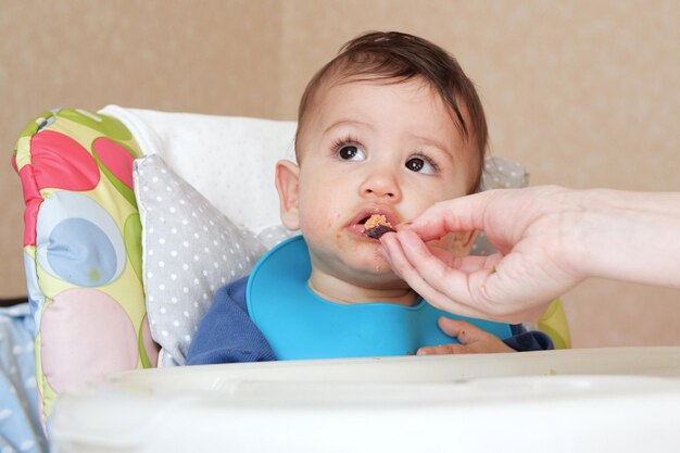 Portret małego chłopca jedzenia żywności Dziecko z łyżką w krześle do karmienia Cute baby jedzenia pierwszego posiłku