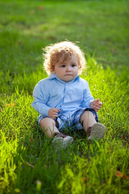 Portret małego chłopca siedzącego na trawie bawiącego się na świeżym powietrzu w trawie