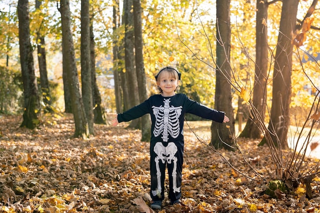 Portret małego chłopca w halloweenowym stroju szkieletowego karnawału na suchych liściach w parku jesienią Wszystkich Świętych Szkolne jesienne święta