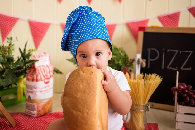 Portret Małego Chłopca W Niebieskim Kapeluszu Szefa Kuchni, Jedzenie Chleba