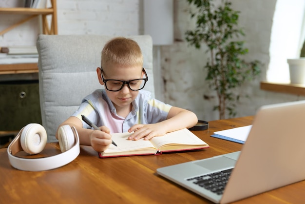 Portret małego chłopca w okularach, uczący się w domu, patrzący na laptopie pracujący z nauczycielem Edukacja online