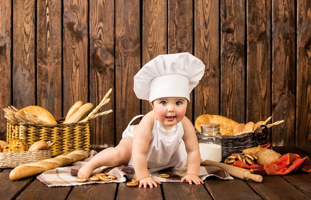 Portret małego dziecka w stroju szefa kuchni wśród produktów piekarniczych na drewnianym tle
