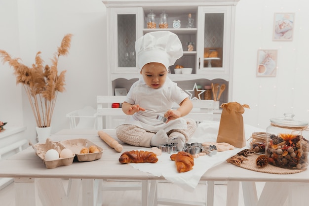 Portret małego kaukaski urocze dziecko w kapeluszu szefa kuchni. Słodkie dziecko siedzi w kuchni w domu.