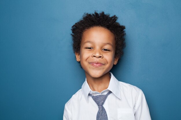 Portret małego mądrego czarnego chłopca uśmiechającego się na niebieskim tle