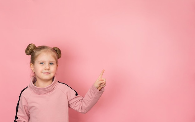 Portret małego uśmiechniętego dziecka dziewczynki na różowym tle, wskazując na miejsce na kopię