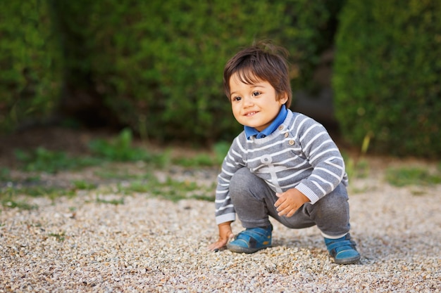 Portret małego wschodniego przystojnego chłopca bawiącego się kamykami na świeżym powietrzu w parku.