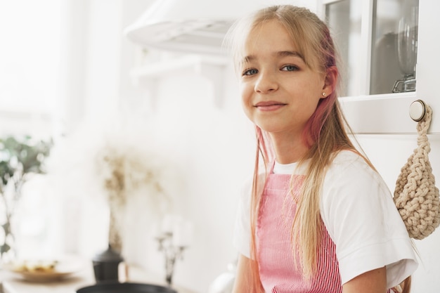 Portret małej blond nastolatki noszącej fartuch w kuchni