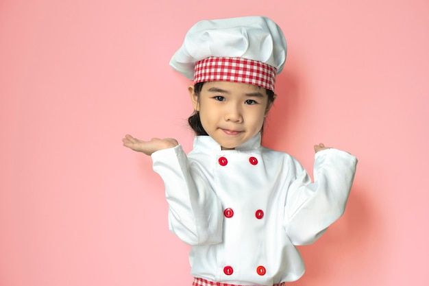 Portret małej dziewczynki kuchennej w białym mundurze izolowanym na różowym tle