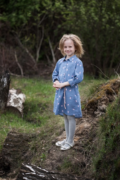 Portret małej kaukaskiej dziewczynki w wieku 5 lat stojącej w lesie i patrzącej w kamerę
