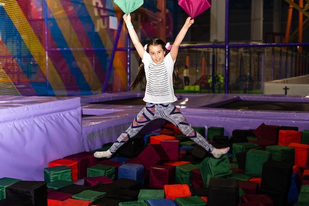 Portret małej słodkiej dziewczynki bawiącej się i skaczącej na trampolinie w pokoju zabaw dla dzieci, krytym placu zabaw. Aktywna dziewczyna bawiąca się w centrum sportowym.