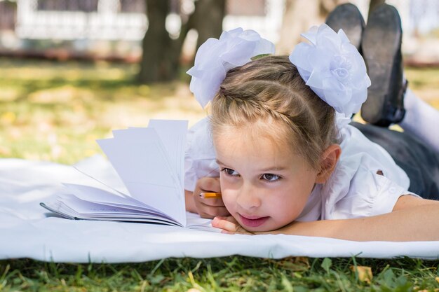 Zdjęcie portret małej uczennicy wykonującej zadanie domowe leżąc na koce w parku jesieniowym