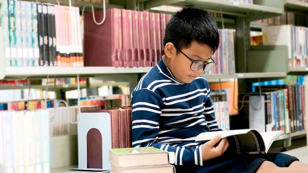 Portret mały azjatykci chłopiec czytanie na bibliotecznej podłoga przy szkołą podstawową.