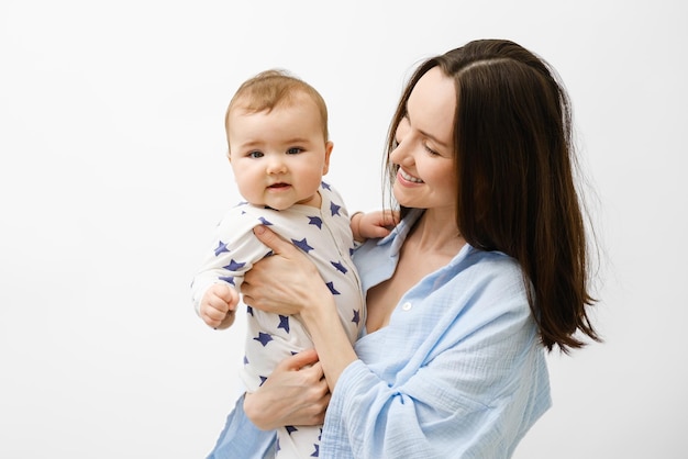 Portret matki i dziecka uśmiechnięta brunetka przytula i trzyma dziecko na białym tle bezwarunkowa koncepcja miłości opieka nad dzieckiem