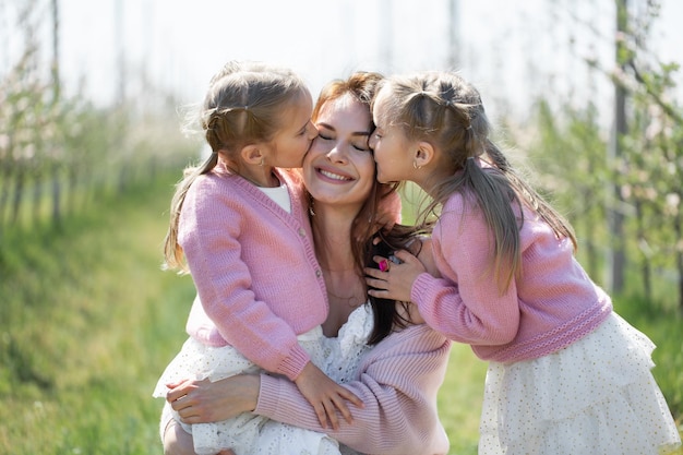 Portret Matki I Jej Córek Bliźniaczek W Kwitnącym Sadzie Jabłkowym Dziewczyny Całują Matkę