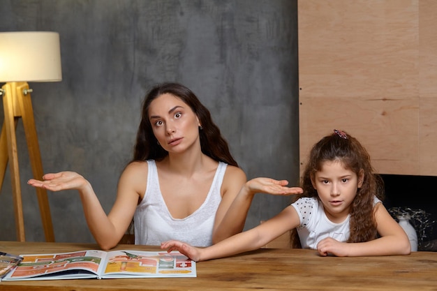 Portret matki pomagającej swojej małej, słodkiej i uroczej córce odrabiać pracę domową w domu, szczęśliwa fa...