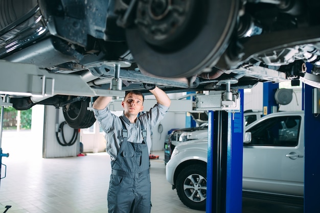 Portret mechanika naprawiającego podniesiony samochód.