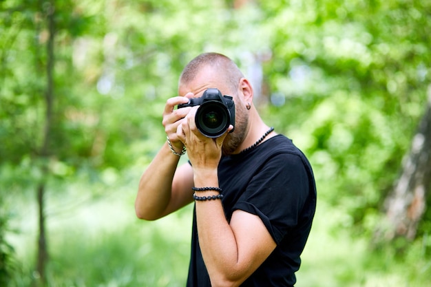 Portret mężczyzny fotografa zakrywającego twarz aparatem na zewnątrz robić zdjęcie, Światowy dzień fotografa, Młody mężczyzna z aparatem w ręku.