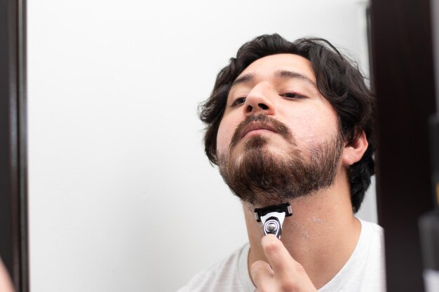 Zdjęcie portret mężczyzny golącego brodę, patrzącego w odbicie w lustrze z miejsca na kopię