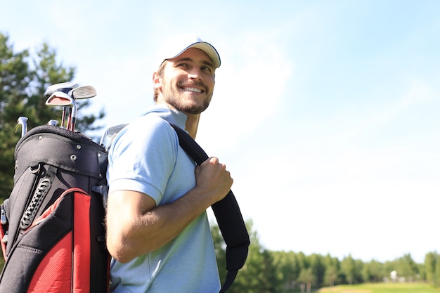 Portret mężczyzny golfisty przewożących torbę golfową podczas spaceru przez zieloną trawę klubu golfowego.