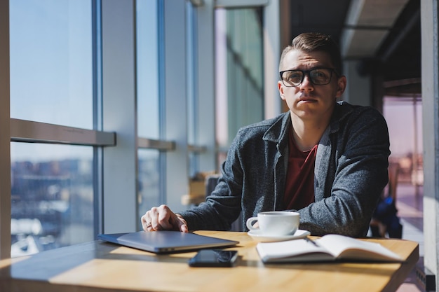 Portret Mężczyzny Informatyka Pracującego Zdalnie Z Nowoczesnym Laptopem Siedzącym Przy Stole I Uśmiechającym Się Do Kamery Podczas Przerwy, Szczęśliwym Programistą W Okularach Do Korekcji Wzroku