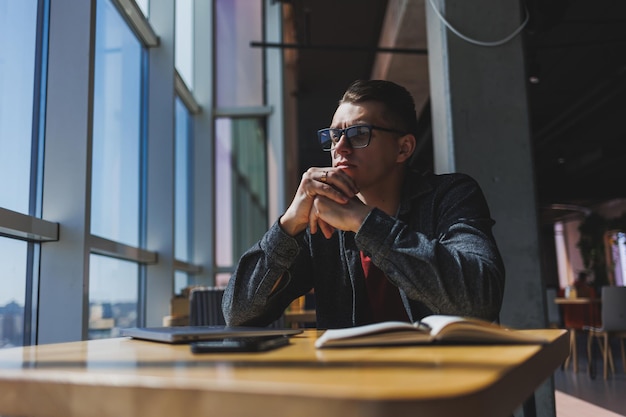 Portret mężczyzny informatyka pracującego zdalnie z nowoczesnym laptopem siedzącym przy stole i uśmiechającym się do kamery podczas przerwy, szczęśliwym programistą w okularach do korekcji wzroku