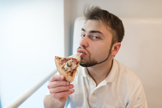 Portret Mężczyzny, Który Zjada Kawałek Pizzy I Patrzy W Kamerę. Mężczyzna Z Brodą Lubi Smak Gorącej Pizzy