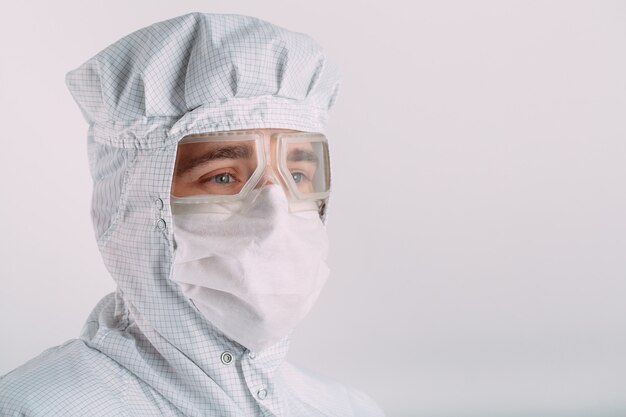 Portret mężczyzny o Europejskim wyglądzie w masce medycznej, okularach ochronnych i kombinezonie chemicznym.